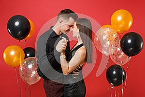 Stunning young couple in black clothes celebrating birthday holiday party on bright red background air balloons