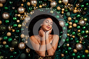 Stunning young woman touching her neck lying on emerald silk texture cloth decorated with christmas glitter baubles