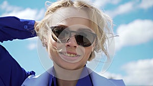 Stunningly beautiful young blond woman in a white dress and aviator sunglasses backlit by sunshine