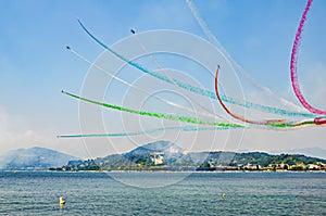 Stunt airplanes performing airshow above a lake with colorful smoke trails. Frecce Tricolore above Lago Maggiore. 25/08/2018 -