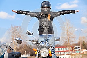 Stunt girl balancing while riding motorcycle without hands, arms extended sidewards
