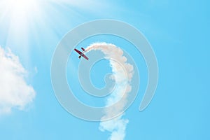 Stunt plane trailing smoke bright sun and clouds