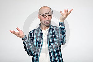 Stupid looking bald man with a grimace on face, wearing slanting glasses and making a strange gesture with hands.