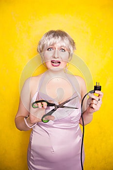 Stupid person cuts electric wire with scissors. silly blonde in pink dress plays bad with electricity on yellow studio