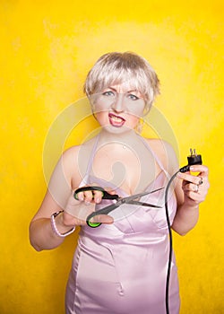 Stupid person cuts electric wire with scissors. silly blonde in pink dress plays bad with electricity on yellow studio