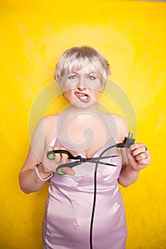 Stupid person cuts electric wire with scissors. silly blonde in pink dress plays bad with electricity on yellow studio