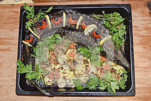 Sturgeon in a baking dish garnished with cherry tomatoes olives and herbs festive dish