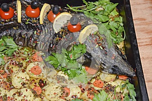 Sturgeon in a baking dish garnished with cherry tomatoes olives and herbs festive dish