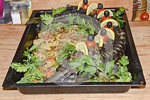 Sturgeon in a baking dish garnished with cherry tomatoes olives and herbs festive dish