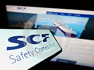 Cellphone with logo of Russian shipping company Sovcomflot (SCF) on screen in front of business website.