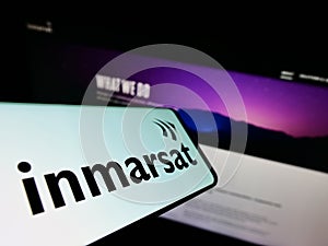 Cellphone with logo of satellite company Inmarsat Global Limited on screen in front of business website.