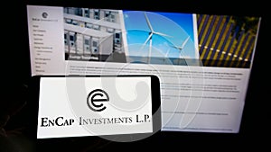 Person holding cellphone with logo of American private equity company EnCap Investments L.P. on screen in front of webpage.