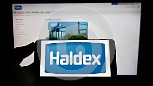 Person holding cellphone with logo of automotive company Haldex Europe SAS on screen in front of business webpage.