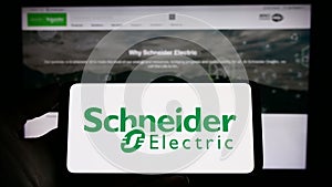 Person holding cellphone with logo of French company Schneider Electric SE on screen in front of business webpage.