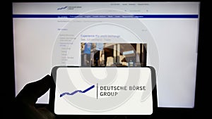 Person holding cellphone with logo of German financial company Deutsche Boerse AG on screen in front of business webpage.