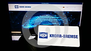 Person holding cellphone with logo of German manufacturing company Knorr-Bremse AG on screen in front of business webpage.
