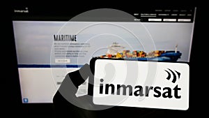 Person holding cellphone with logo of satellite company Inmarsat Global Limited on screen in front of business webpage.