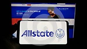 Person holding cellphone with logo of US insurance company The Allstate Corporation on screen in front of web page.