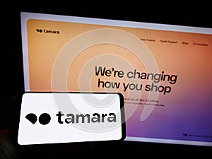 Person holding mobile phone with logo of fintech company Nakhla IT Systems LLC (Tamara) on screen in front of web page.