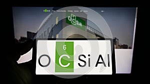 Person holding mobile phone with logo of Luxembourgish company OCSiAl on screen in front of business web page.