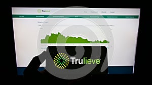 Person holding mobile phone with logo of medical marijuana company Trulieve Cannabis Corp. on screen in front of web page.