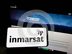 Person holding mobile phone with logo of satellite company Inmarsat Global Limited on screen in front of business web page.