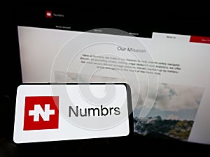 Person holding mobile phone with logo of Swiss fintech company Numbrs Personal Finance AG on screen in front of web page.