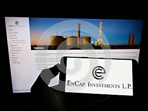 Person holding mobile phone with logo of US private equity company EnCap Investments L.P. on screen in front of web page.