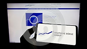 Person holding smartphone with logo of German financial company Deutsche Borse AG on screen in front of business web page.