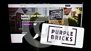 Person holding smartphone with logo of real estate company Purplebricks Group plc on screen in front of website.