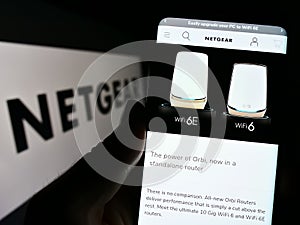 Person holding smartphone with website of US computer networking company Netgear Inc. on screen in front of logo.