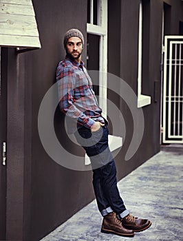 Style and class early in the morning. a handsome young man leaning against a wall posing with his hands in his pockets