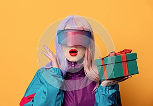 Style woman in VR glasses and 90s sport suit hold gift box on yellow background