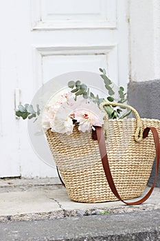 Styled stock photo. Feminine wedding still life composition with straw French basket bag with pink peonies flowers and