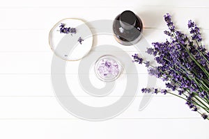 Styled summer beauty composition. Essential, massage oil, lavender flowers bouquet, bath salt on white wooden table