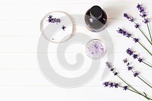 Styled summer beauty composition. Essential, massage oil, purple lavender flowers and bath salt on white wooden table