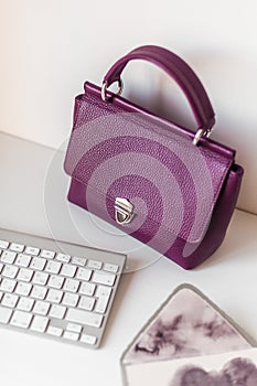 Styled violet lifestyle fashion leather bag surrounded by apple keyboard and lux stationery on minimal white background