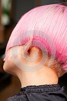 Styling and cutting dyed pink hair of young model back view in a hairdressing salon. Pink short hairstyle.