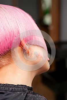 Styling and cutting dyed pink hair of young model back view in a hairdressing salon. Pink short hairstyle.