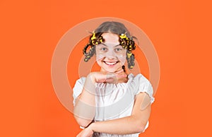 Styling tips. Teen hobbies. Small girl Curling Hair Using Curlers orange background. Daughter with curlers on her head