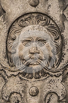 Stylised bearded man`s face carved into a stone wall shot straight on.