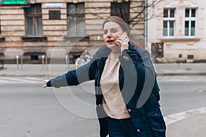 Stylish 30s woman with backpack catching a taxi. Woman doing multiple tasks. Middle age woman talking on smartphone and