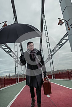 stylish adult man with umbrella and luggage walking photo