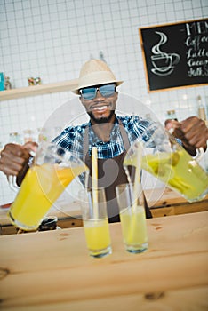 stylish african american bartender pouring lemonades into glasses on bar counter