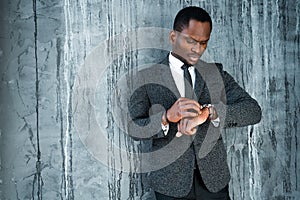 Stylish African American businessman in a suit looking seriously at the watch on his hands in a hurry