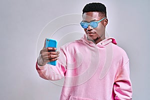 Stylish african american man wearing blue glasses holding a blue phone. Conceptual creativity and fashion, gadgets and ideas