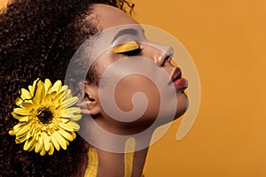 Stylish african american woman with artistic make-up and gerbera in hair dreaming