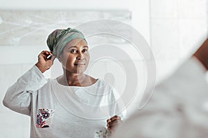 Stylish African woman putting on a headscarf in the mirror