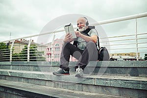 Stylish aged man in headphones scrolling something in tablet com
