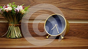 Stylish alarm clock and a small bouquet of artificial flowers on the bedside table